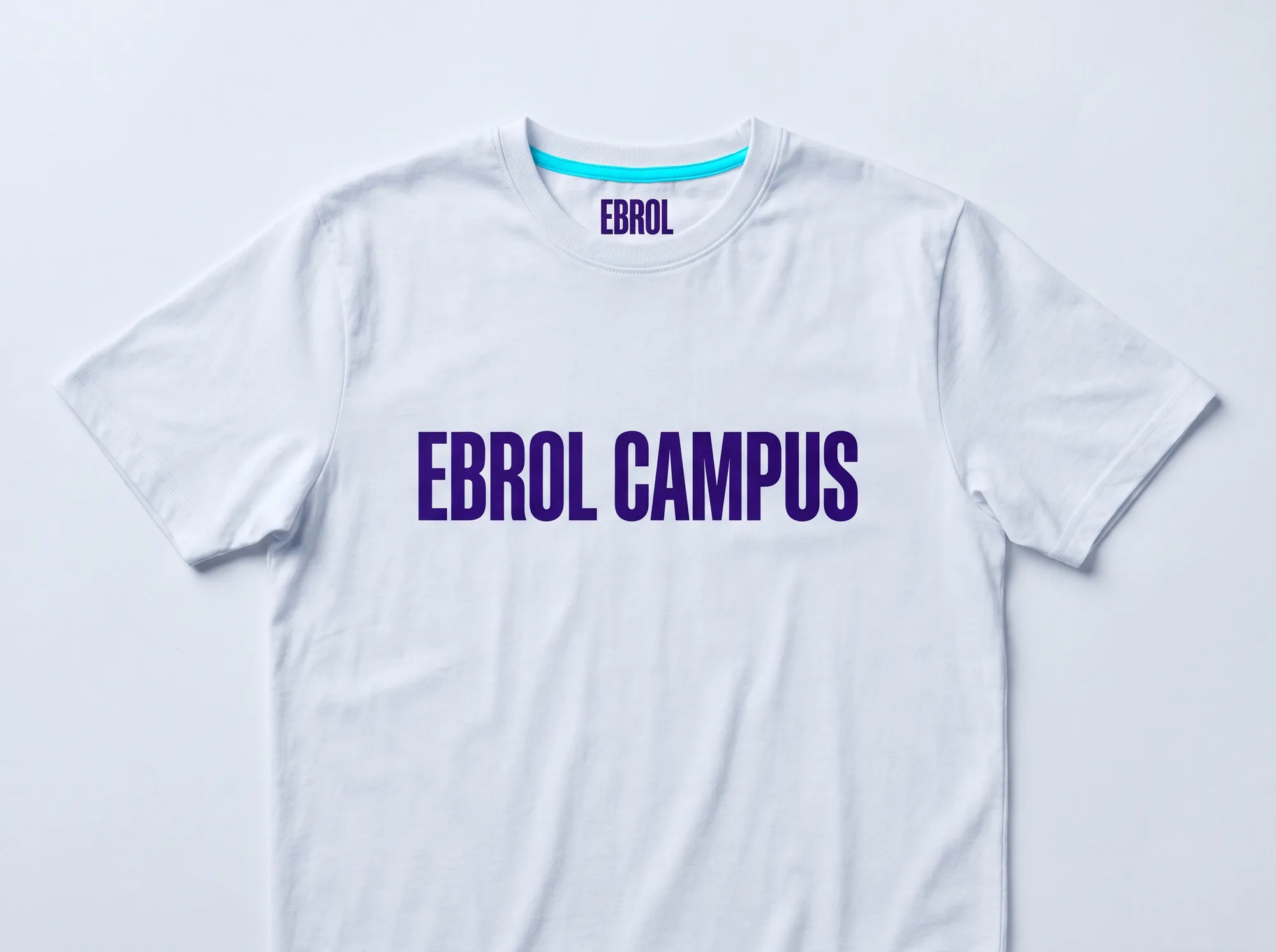 Ebrol Campus Engineer Tee (Apparel) — A working campus-engineer cotton tee — cool near-white (#FAFAFB) with EBROL CAMPUS printed in deep violet (#2A1240) Space Grotesk bold caps across the chest, electric cyan (#00E5C5) accent on the back.