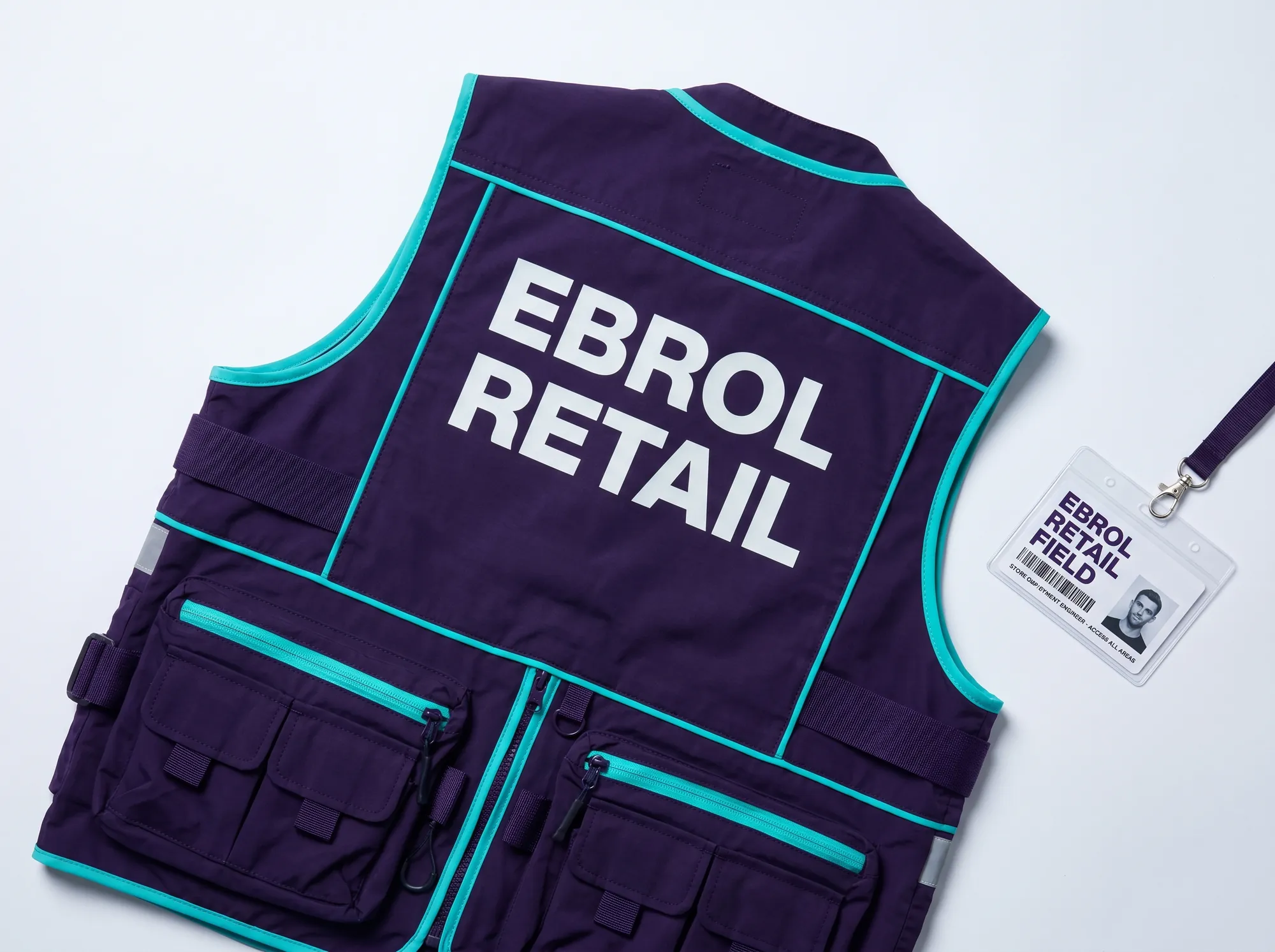 Ebrol Retail Engineer Vest (Apparel) — A working store-side engineer field vest — deep violet (#2A1240) heavy nylon with EBROL RETAIL printed in cool near-white (#FAFAFB) Space Grotesk bold caps on the back, electric cyan (#00E5C5) accent piping. Worn during in-store deployment visits.